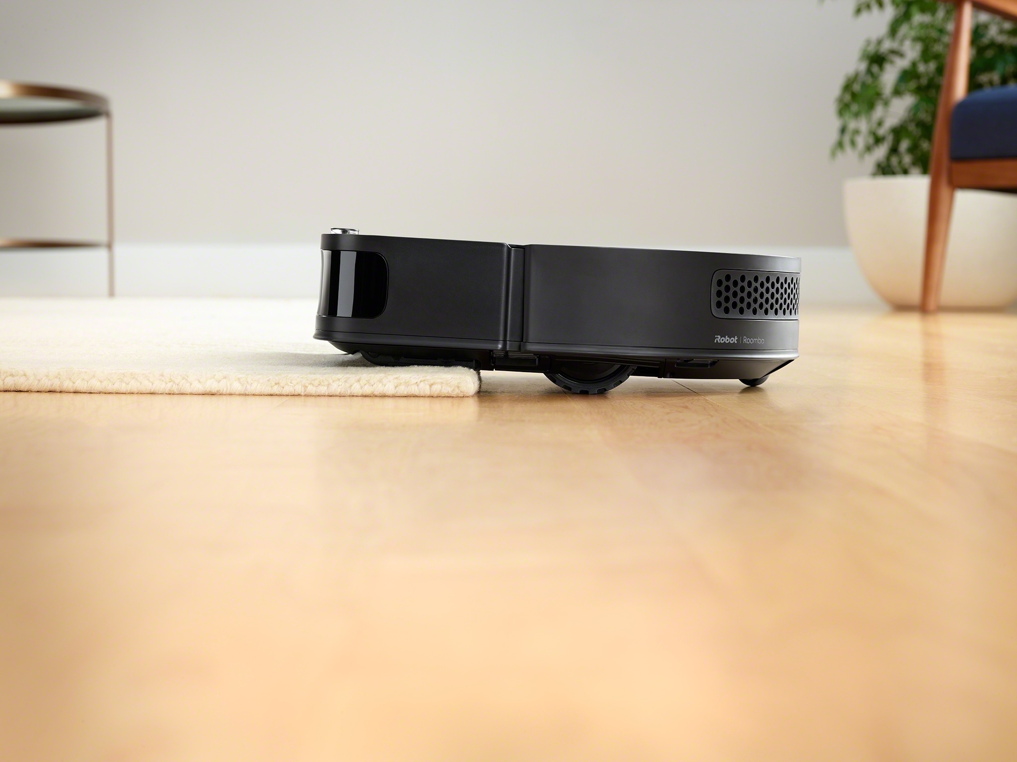 A Roomba vacuum robot drives over a thick rug in a modern looking living room.