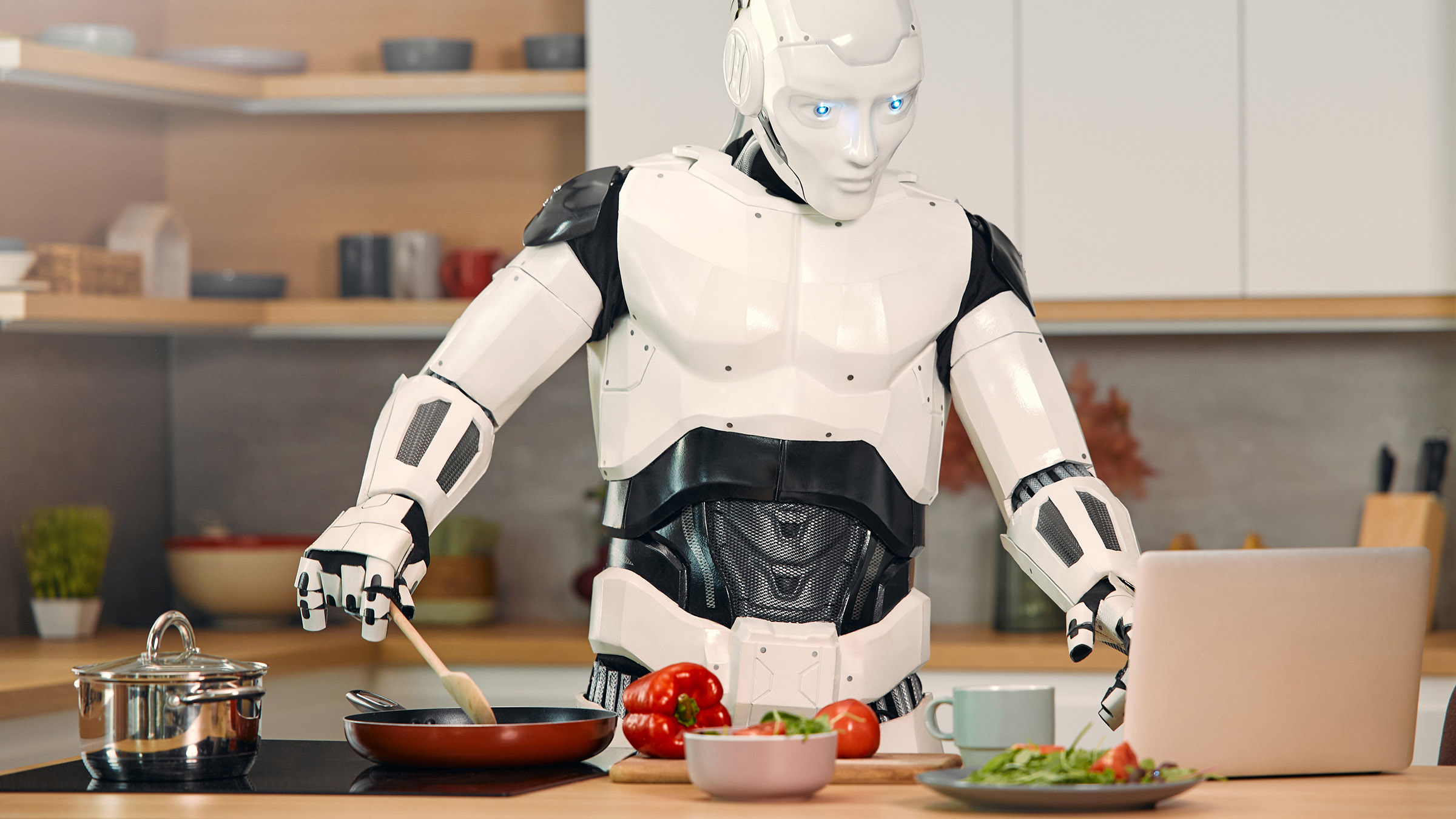 A digital illustration shows a humanoid robot with black and white body cooking in a kitchen by following a recipe on a screen, with a wooden spatula on its hands and red peppers and other vegetables on the counter.