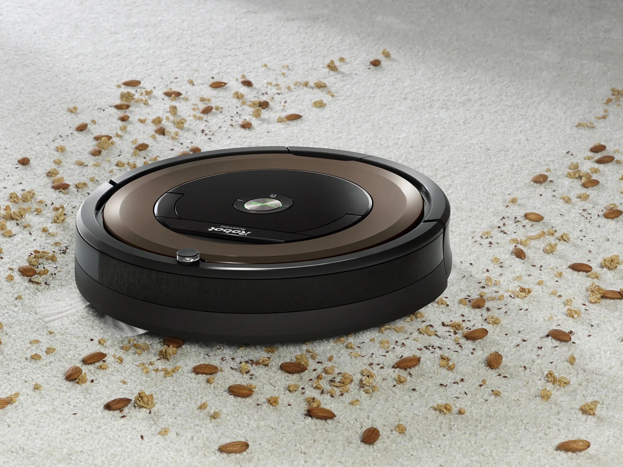 A Roomba robot vacuums almonds and other debris from a white carpet.