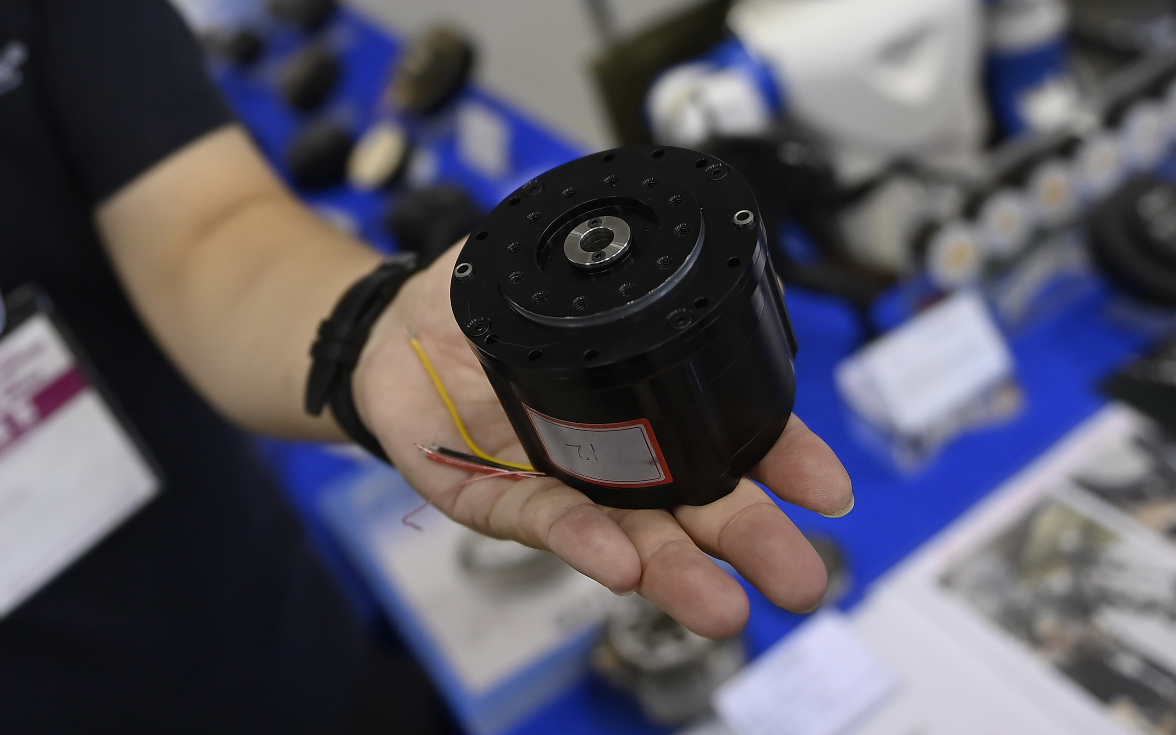 A cylindrical metal black actuator with wires sticking out rests on a person's palm.