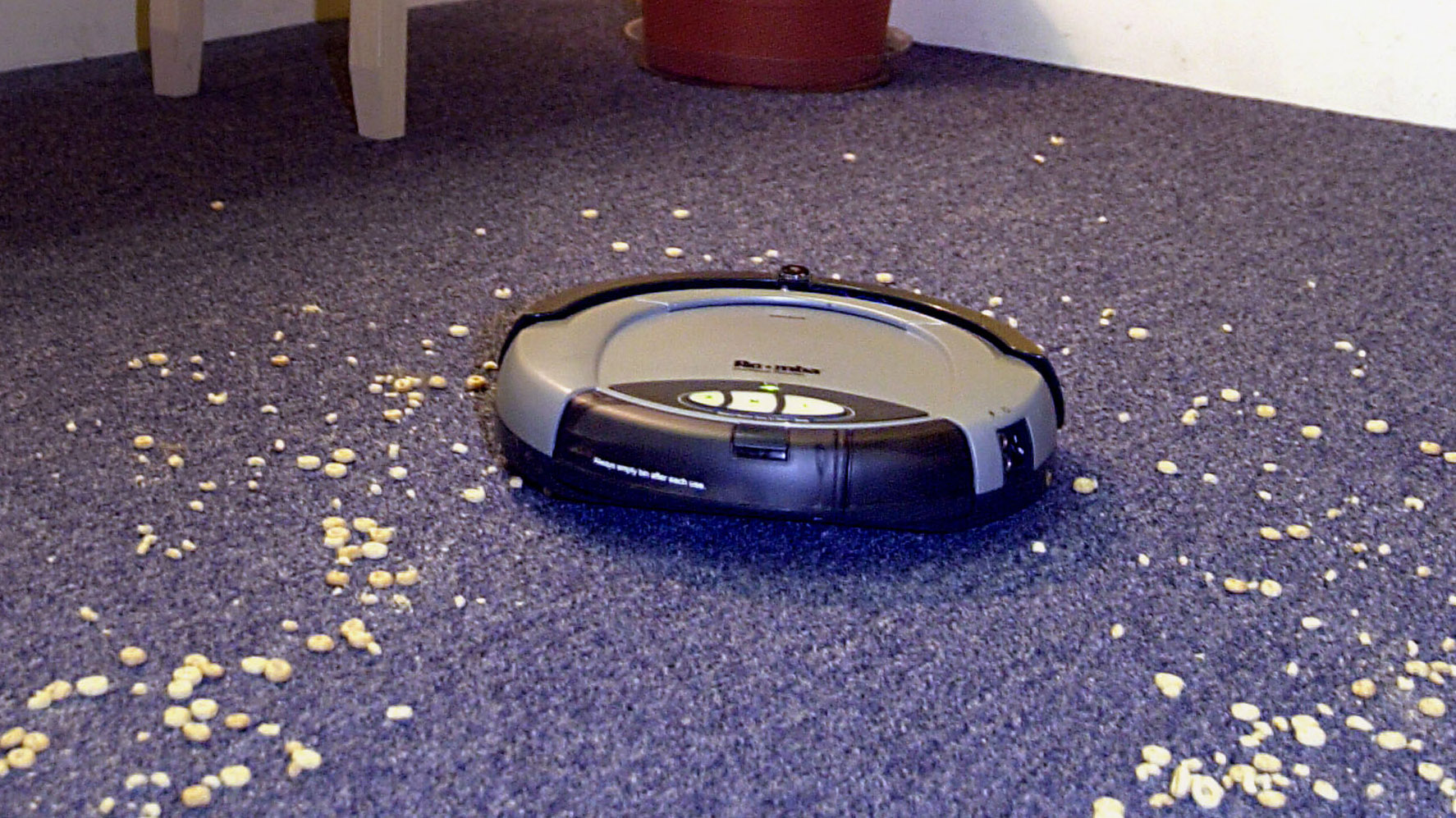 The first version of the Roomba robot vacuums crumbs from a purple carpet.