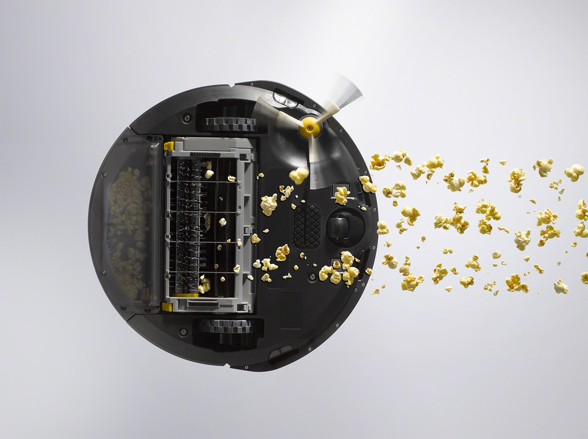 A Roomba vacuuming popcorn seen from below through a transparent surface.